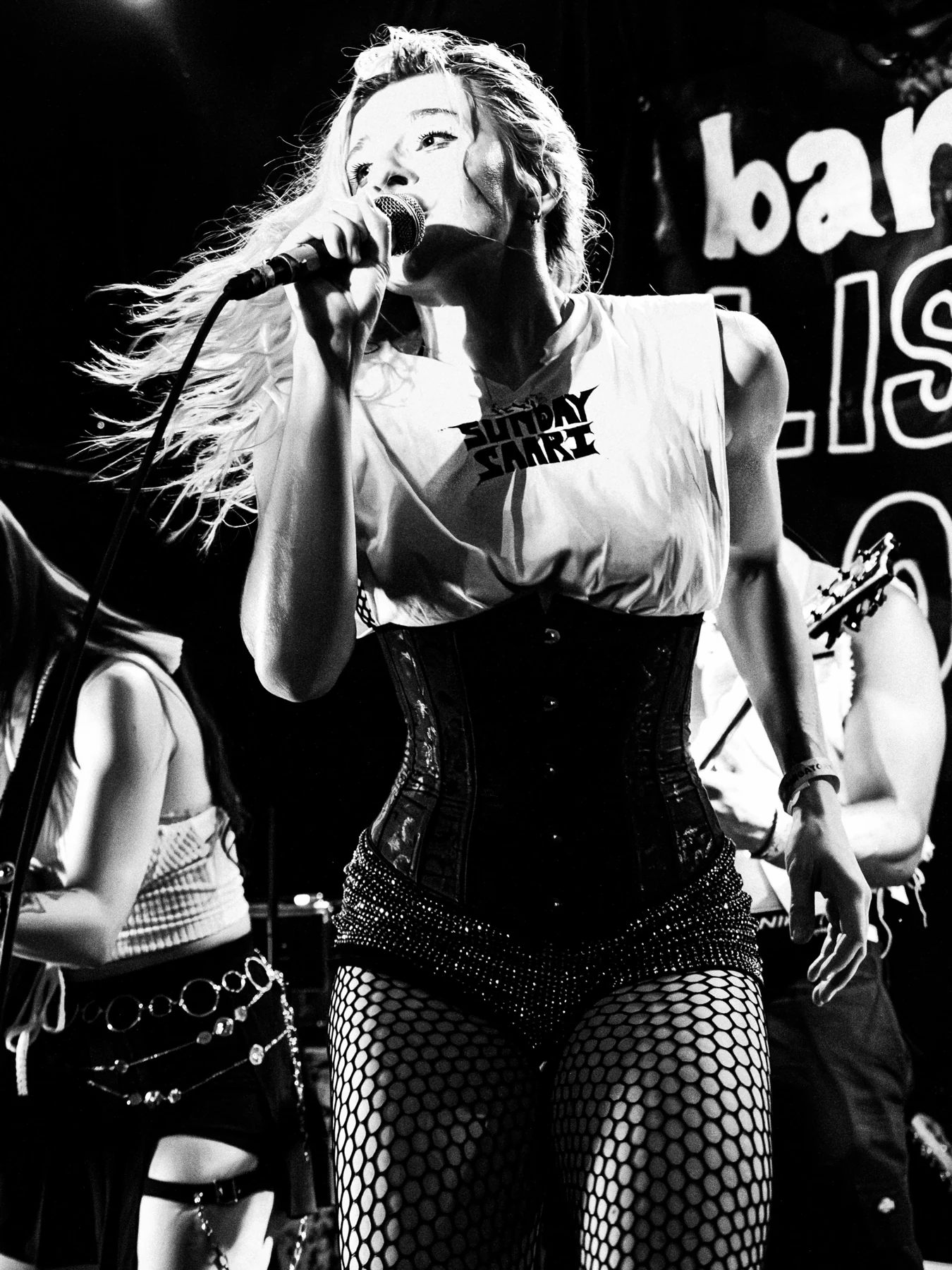 Sunday Saari singing into a microphone onstage, wearing her own Sunday Saari shirt