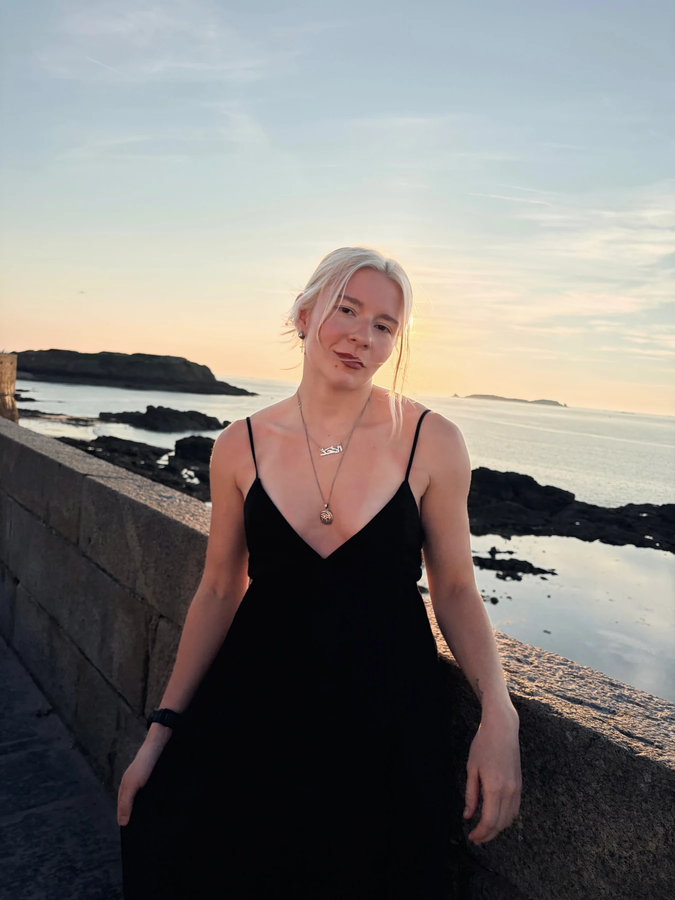 Sunday Saari in a black dress by the sea at sunset